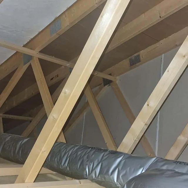Loft med trekonstruksjon, isolasjon og en ventilasjonskanal i plast.