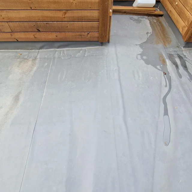 Grått, vanntett takbelegg med trepanel rundt. Noe vannsig og en sko synlig nederst i bildet.